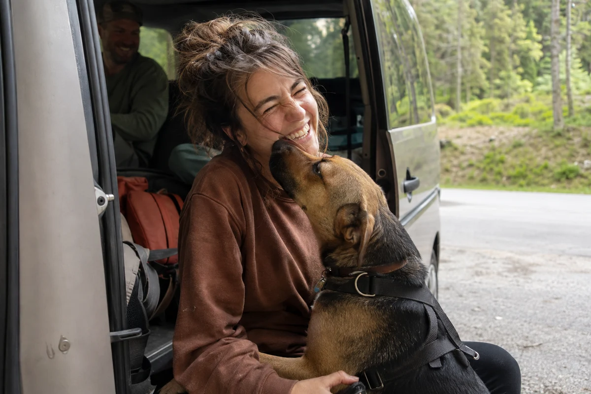 A woman laughing and hugging her dog by the open car door during a rest stop